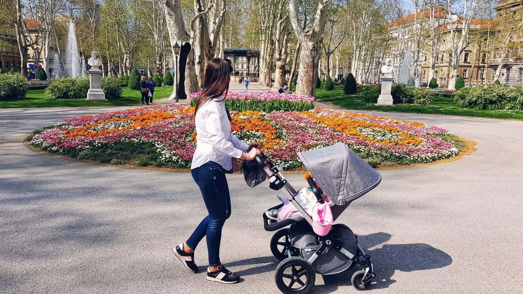 young mother walking with a baby stroller on a beautiful sunny day in park with beautiful flower beds t20 xvKGxl